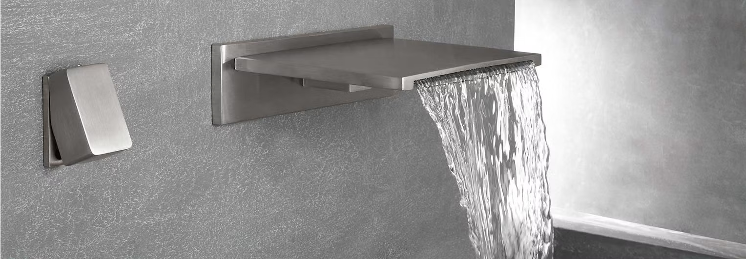Rubinetto moderno a parete che versa acqua in un lavandino contro una parete grigia con superficie ruvida.