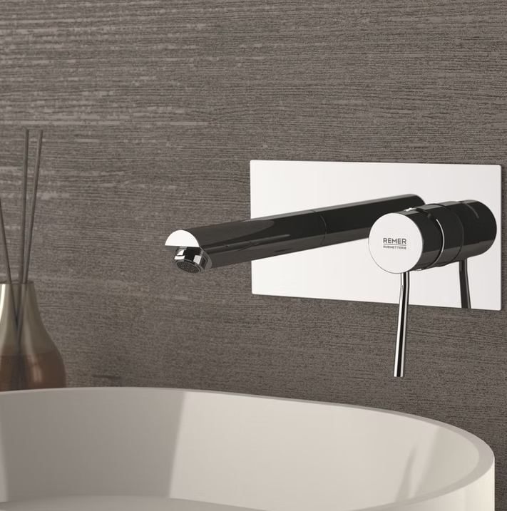 Rubinetto a parete moderno cromato sopra un lavabo bianco su piastrelle grigie con texture.