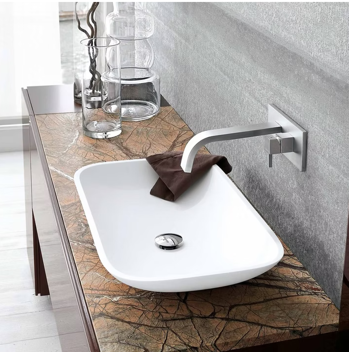 Lavabo da bagno moderno con piano in pietra, rubinetto a parete e asciugamano marrone appoggiato sul beccuccio.