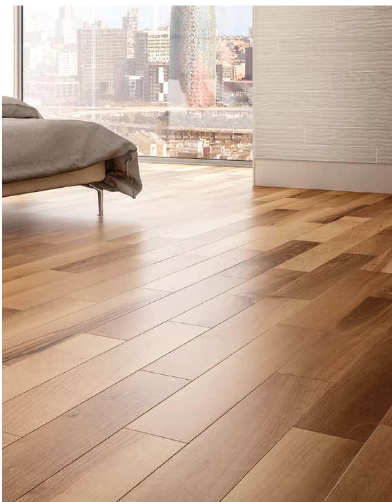 Camera da letto luminosa con letto e pavimento in legno accanto a una finestra con vista sugli edifici della città.