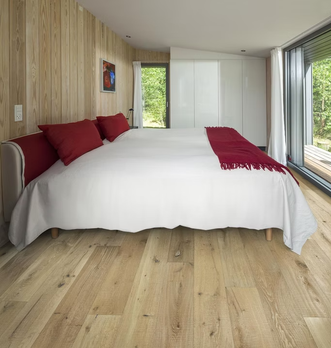 Camera da letto moderna con letto bianco, dettagli rossi, pareti e pavimento in legno, ampie finestre e luce naturale.