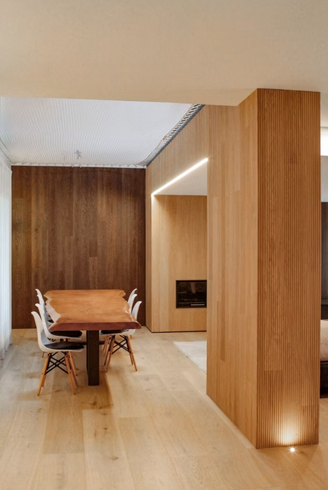 Sala da pranzo moderna con pareti rivestite in legno, pavimento in legno chiaro e tavolo da pranzo con sedie.