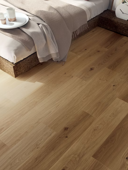 Pavimento in legno chiaro accanto a un letto con lenzuola beige e un vassoio da comodino con tazza e piattino.