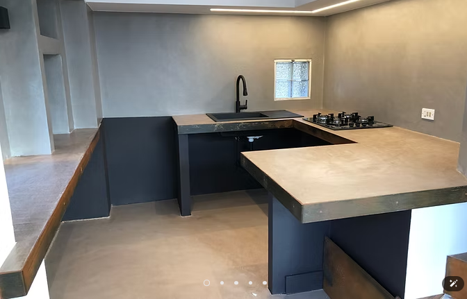 Cucina moderna grigia con ripiani neri, penisola, lavello e piano cottura a gas sotto una finestra a muro.