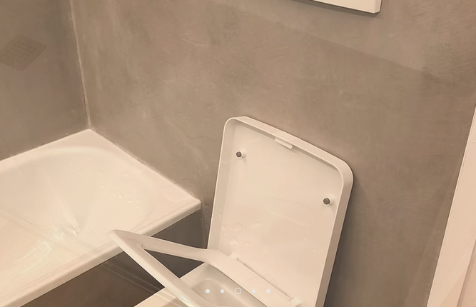 Sedile del water aperto in un piccolo bagno beige accanto alla doccia o alla vasca.