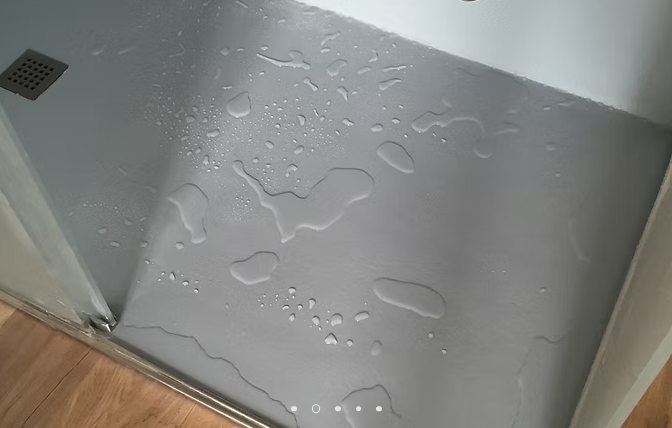 Pavimento grigio bagnato con pozzanghere sparse accanto a una porta e battiscopa in legno.