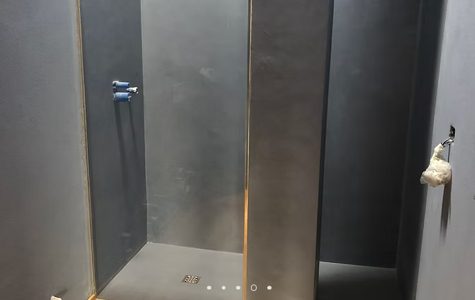 Interno di una toilette buia con porte grigie e un rotolo di carta igienica appeso sulla destra.