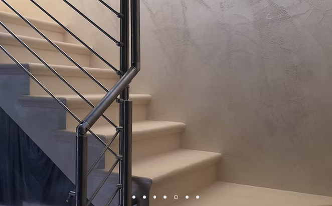Scala moderna con ringhiera in metallo nero e gradini beige su una parete texturizzata.