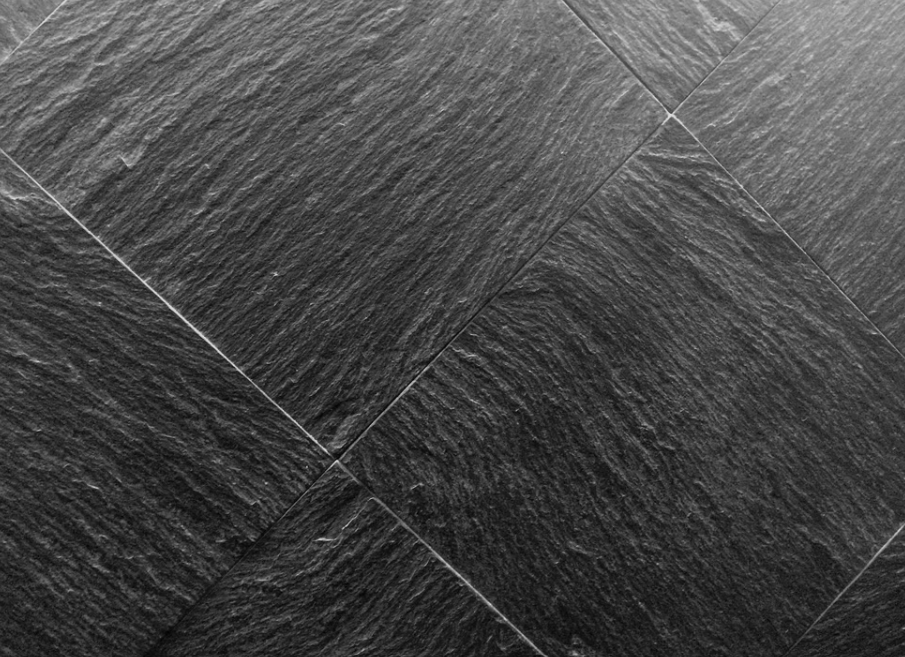 Superficie in pietra o ardesia grigio scuro con texture e linee di piastrelle diagonali
