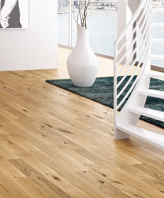 Pavimento in legno chiaro con un vaso bianco su un tappeto scuro accanto a una scala bianca vicino a grandi finestre
