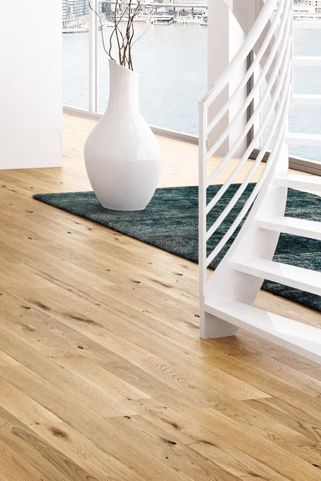 Scala moderna bianca su pavimento in legno chiaro con un grande vaso bianco e un tappeto verde scuro in un interno luminoso