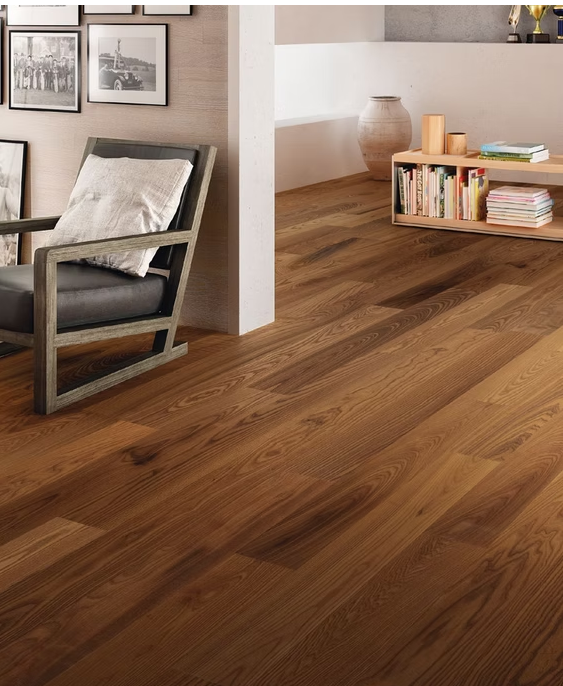 Soggiorno moderno con pavimento in legno, poltrona grigia, quadri alle pareti e libreria bassa.