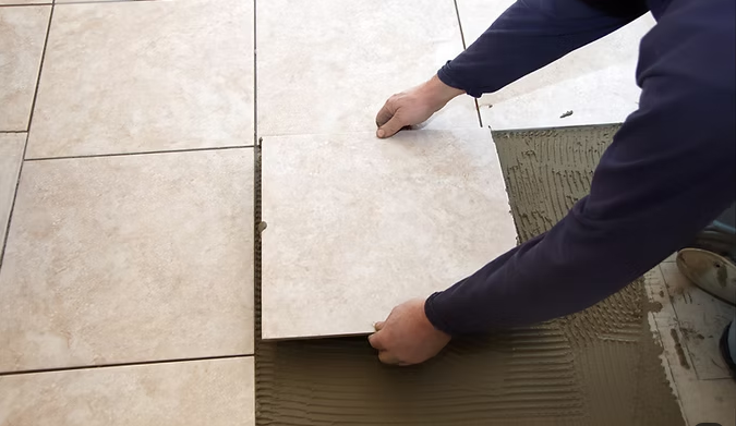 Mani che posano una piastrella beige su malta adesiva sottile su un pavimento