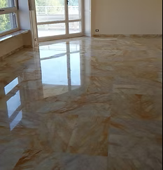 Stanza vuota con piastrelle lucide, grandi finestre e luminosi riflessi sul pavimento.