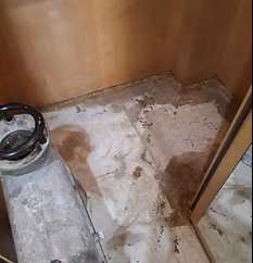 Pavimento danneggiato in un piccolo armadio o ripostiglio in legno, con macchie e detriti sul pavimento.