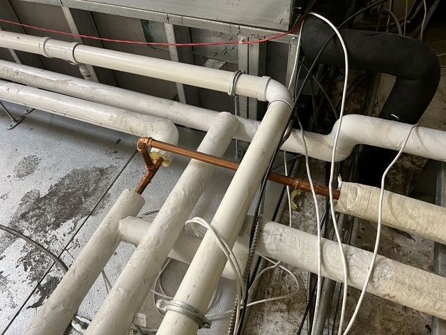 White pipes and cables in a utility area, with rust-stained joints and a concrete wall.