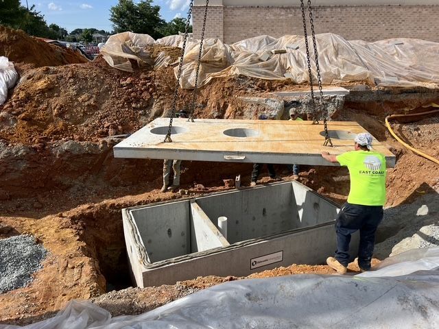 Worker in neon shirt installing a concrete utility vault at a construction site