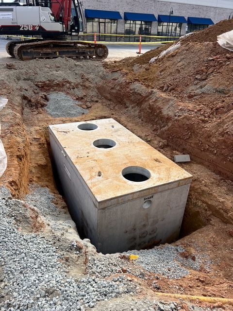 Concrete utility vault in an excavated construction trench beside heavy equipment