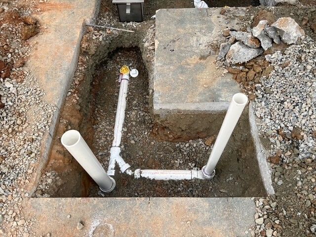 White PVC pipes installed in a trench beside a concrete slab and gravel soil