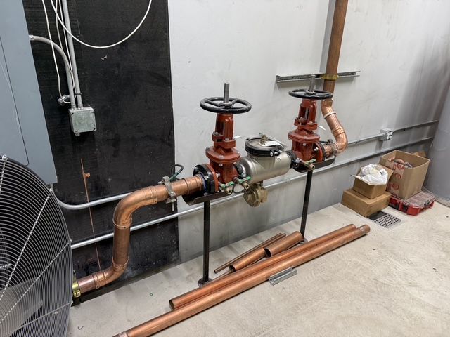 Industrial pipes and red valve assemblies along a wall in a utility room