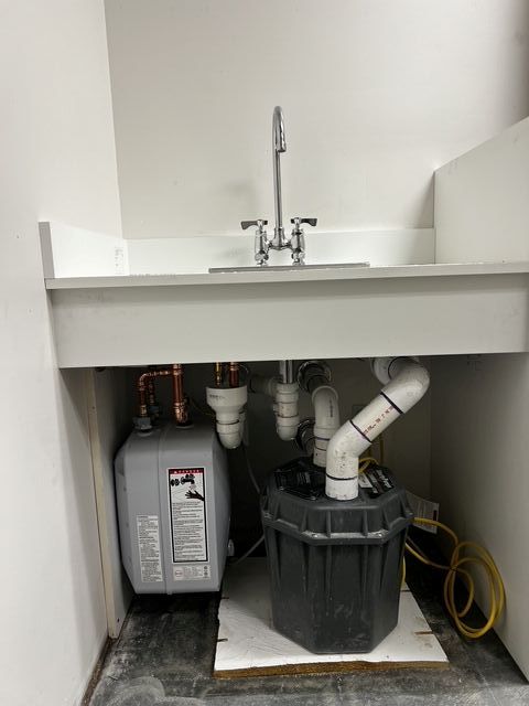 Undersink utility cabinet with exposed plumbing, gray pump unit, and coiled yellow hose
