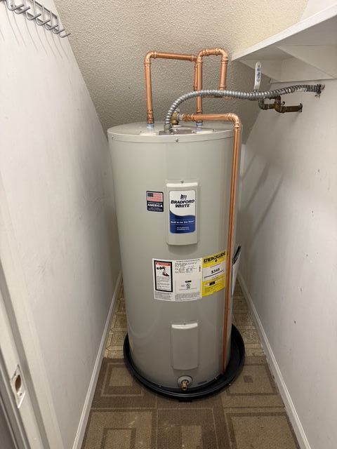 Water heater in a narrow utility closet with copper pipes and warning labels.