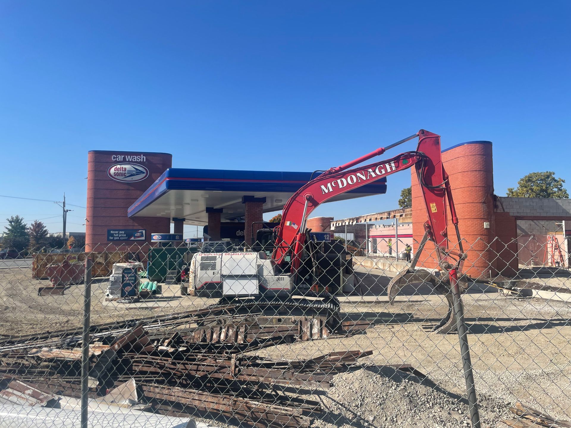A red excavator is sitting in front of a gas station.