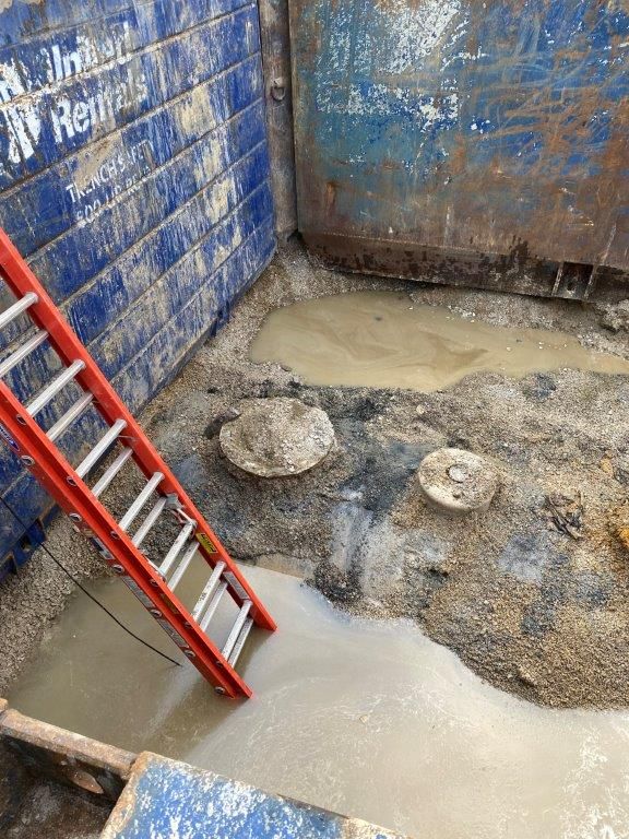 A red ladder is leaning against a blue wall in a muddy area.