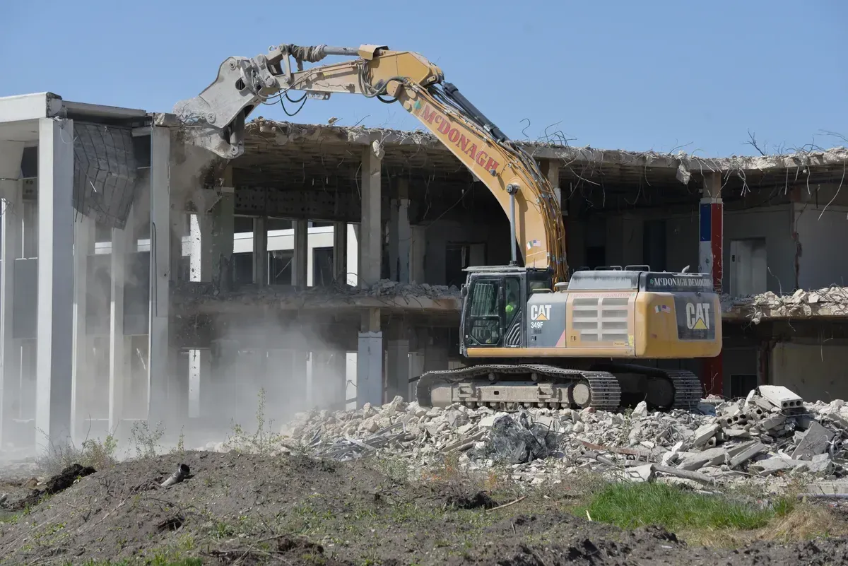 A large yellow excavator is demolishing a large building.