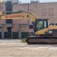 A yellow excavator is parked in front of a brick building.