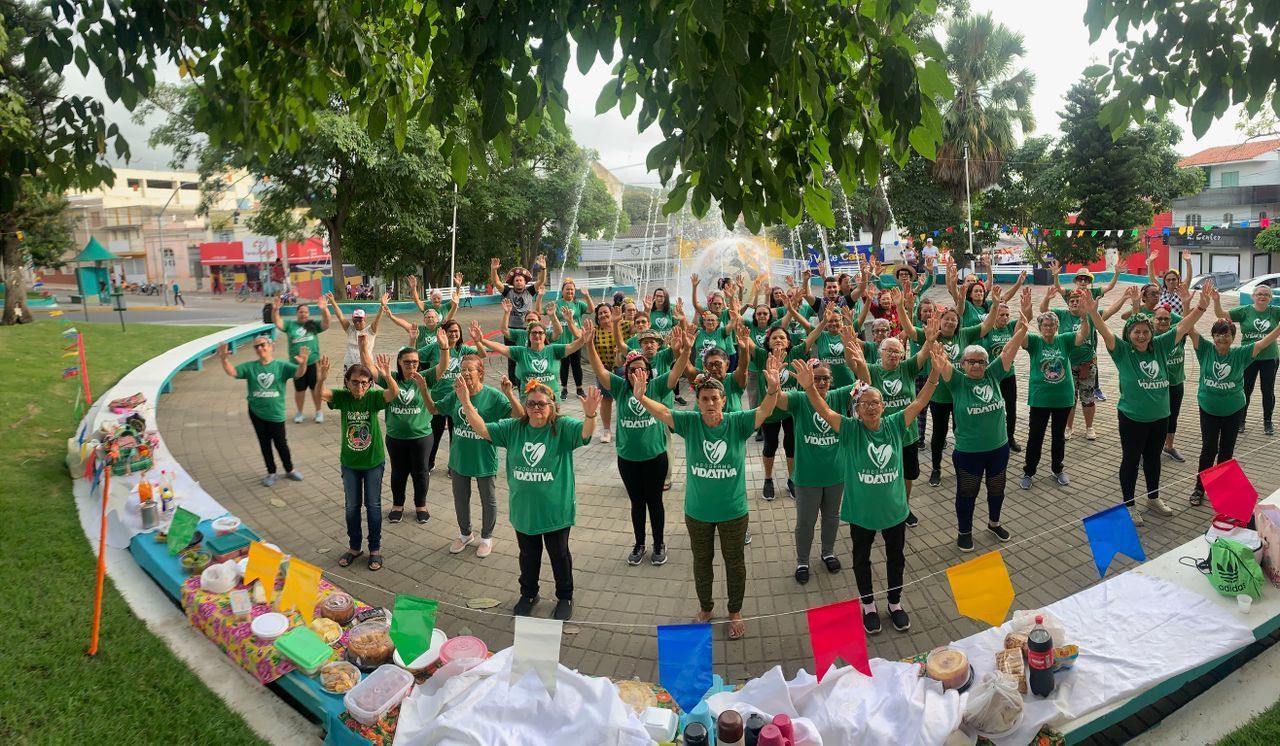 Grupo de pessoas com camisas verdes e braços levantados, reunidas ao ar livre perto de uma fonte.