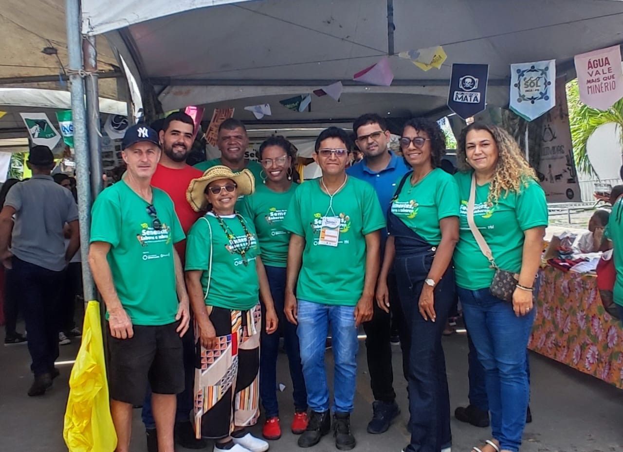 Um grupo de pessoas vestindo camisas verdes iguais está reunido sob uma tenda em um evento ao ar livre.