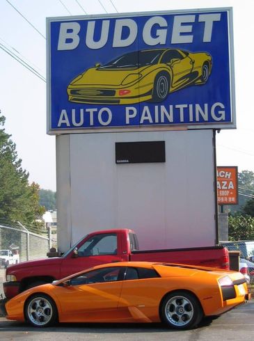 Two sports cars are parked in front of a budget auto painting sign