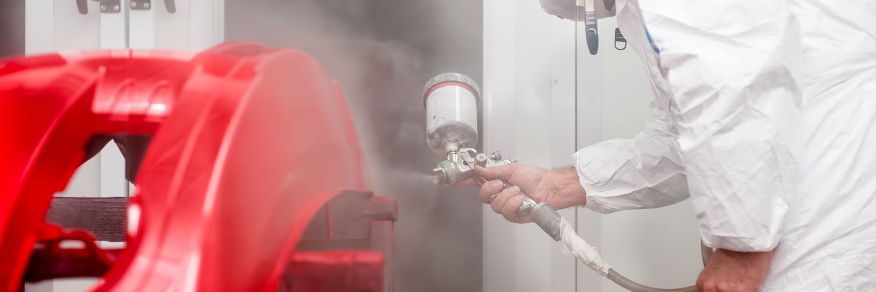 A man in a white suit is spray painting a red object.