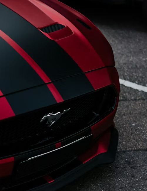 Red and black Ford Mustang with racing stripes on asphalt.