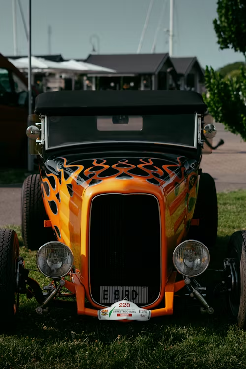 A close up of an orange hot rod parked in the grass.