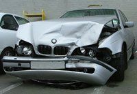 A silver bmw with a damaged front bumper is parked in a parking lot.