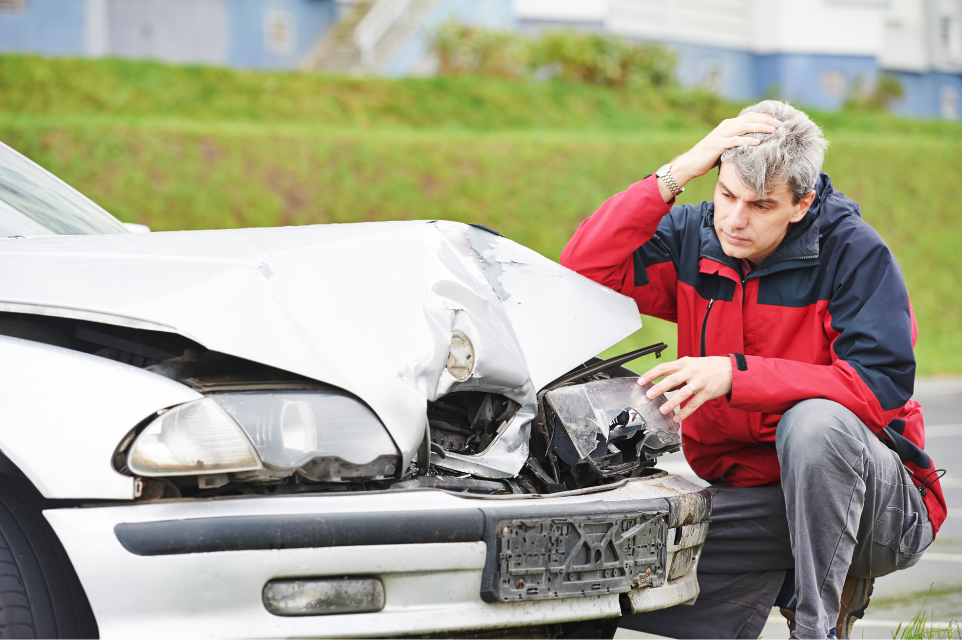 A man is kneeling down in front of a damaged car.
