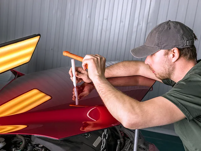 A man is working on the hood of a red car.