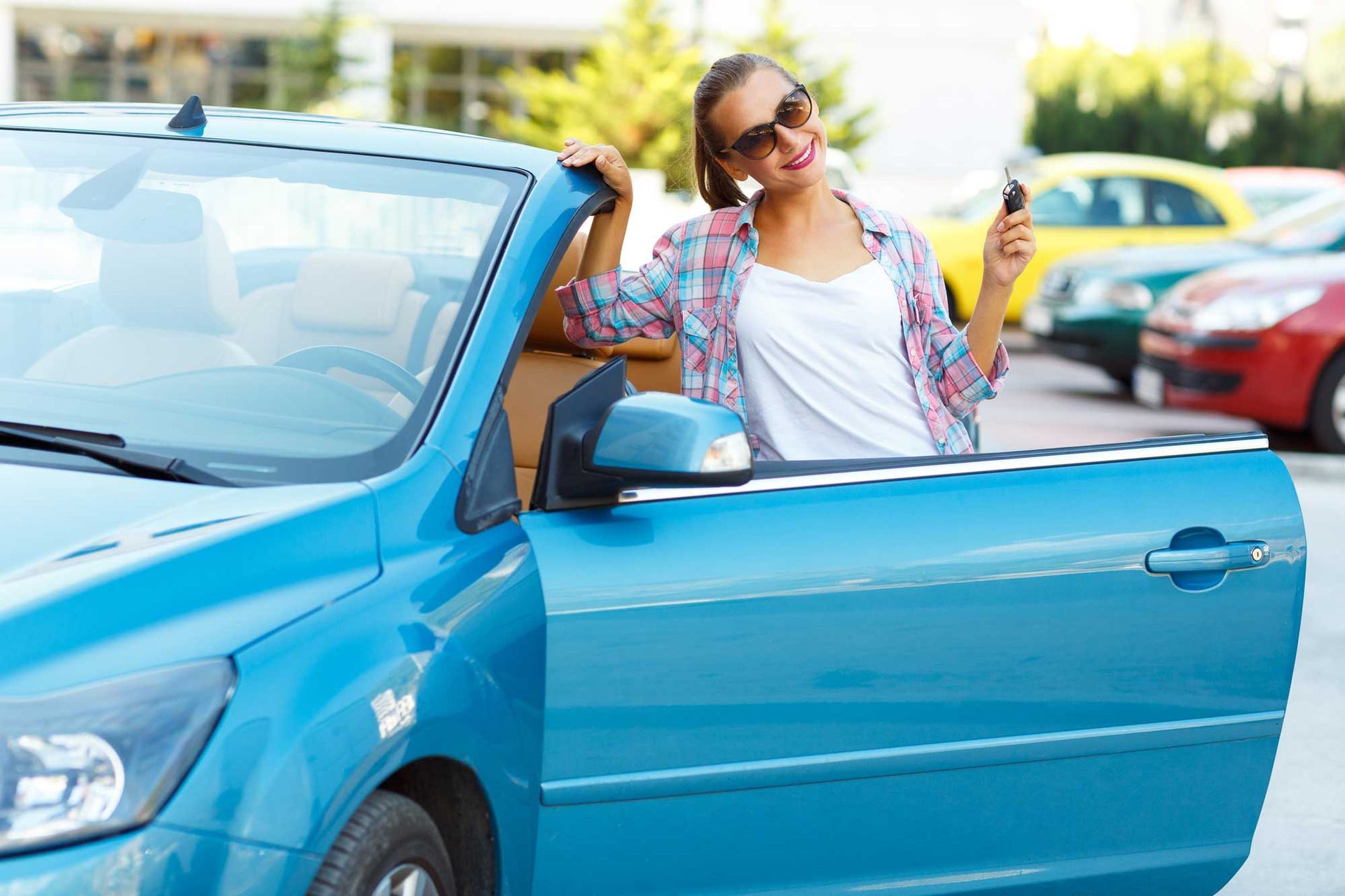 A woman is standing next to a blue car holding a car key.