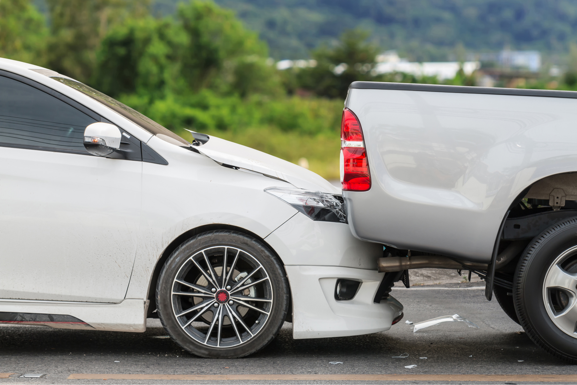 A white car is being towed by a silver truck.