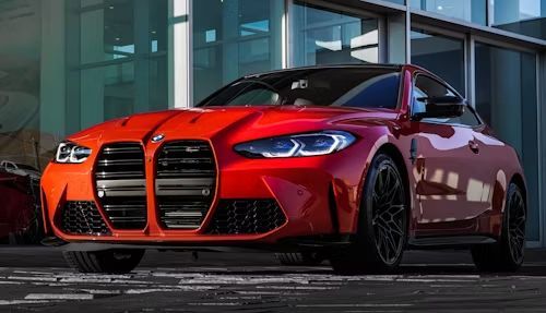 Red BMW M4 coupe parked in front of a modern building with large windows.