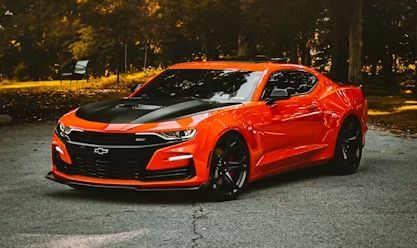 Bright orange sports coupe parked on a road at night in a wooded area