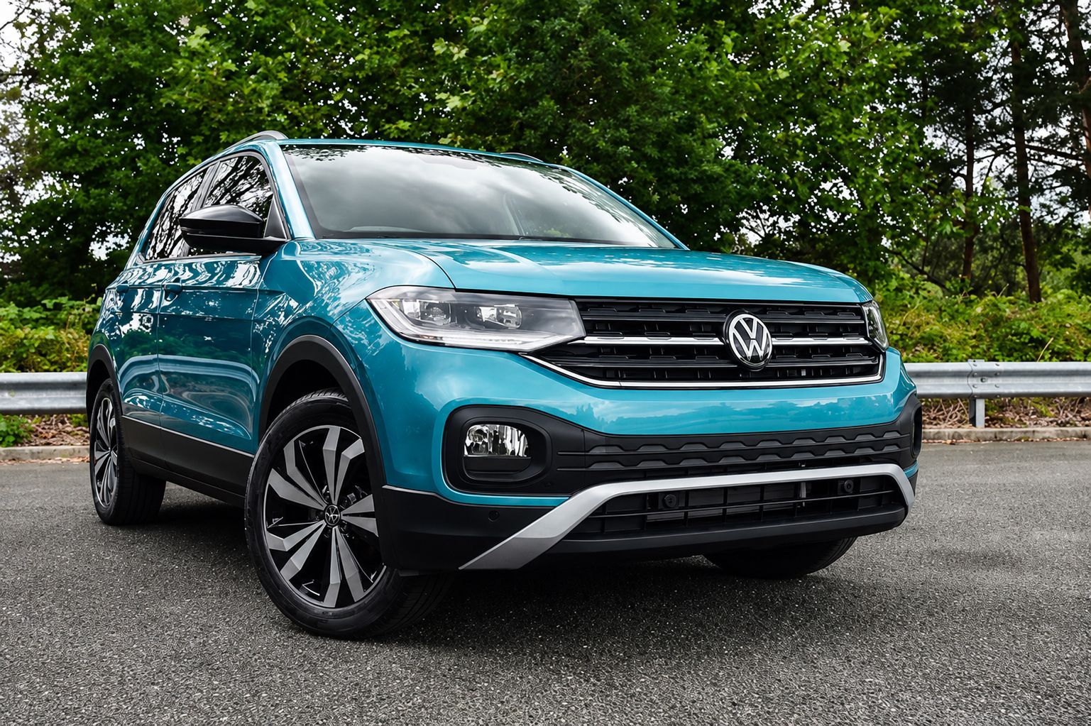 Teal Volkswagen SUV parked on a road with trees and guardrail in the background