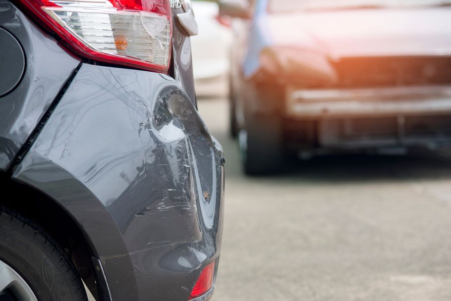Gray car with rear-end damage, hit by a dark-colored car in a parking area.