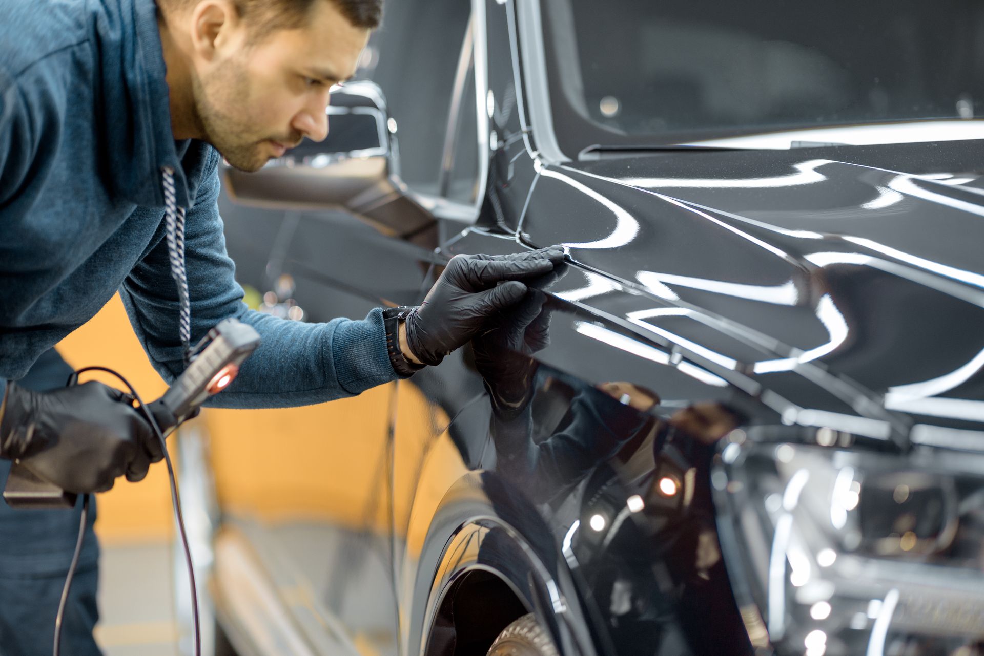 Technician inspecting a black car's body panel during professional auto body repair.