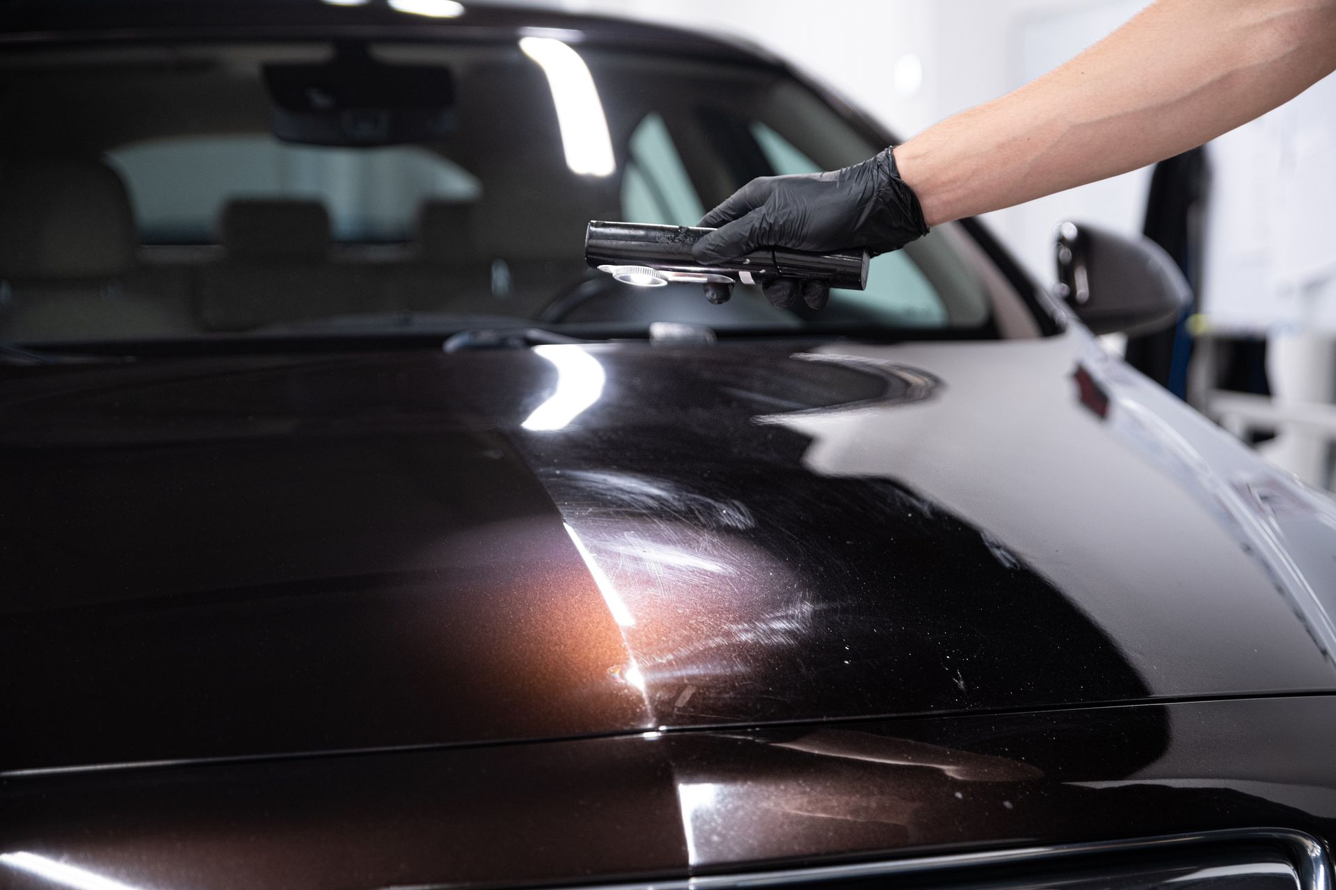 Hand with black glove applying polish to a car hood, revealing shiny finish.