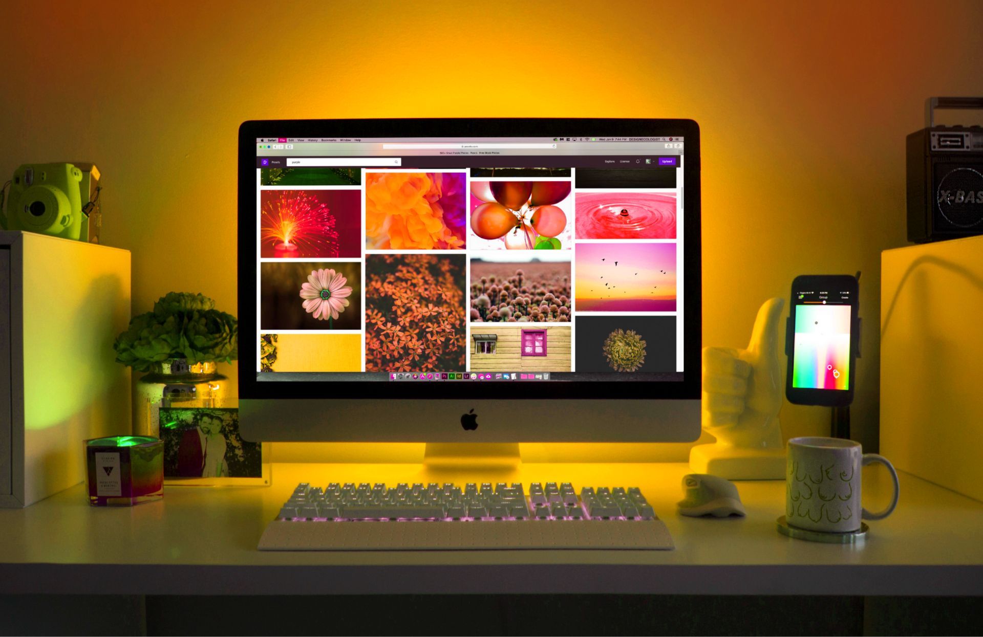 Desk setup with iMac, keyboard, phone, mug, and warm yellow lighting