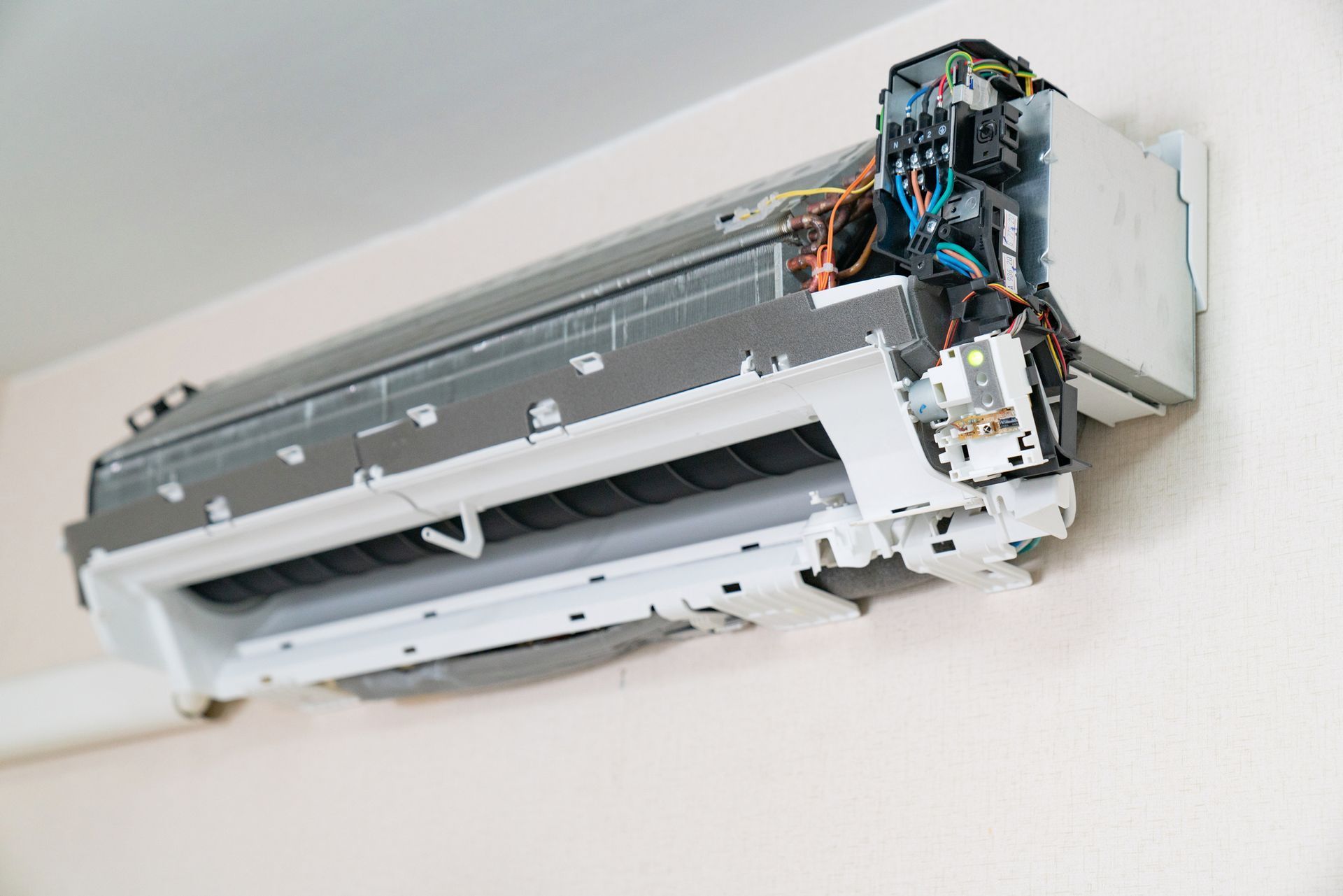 White and gray air conditioner unit mounted on a beige wall, partially disassembled.