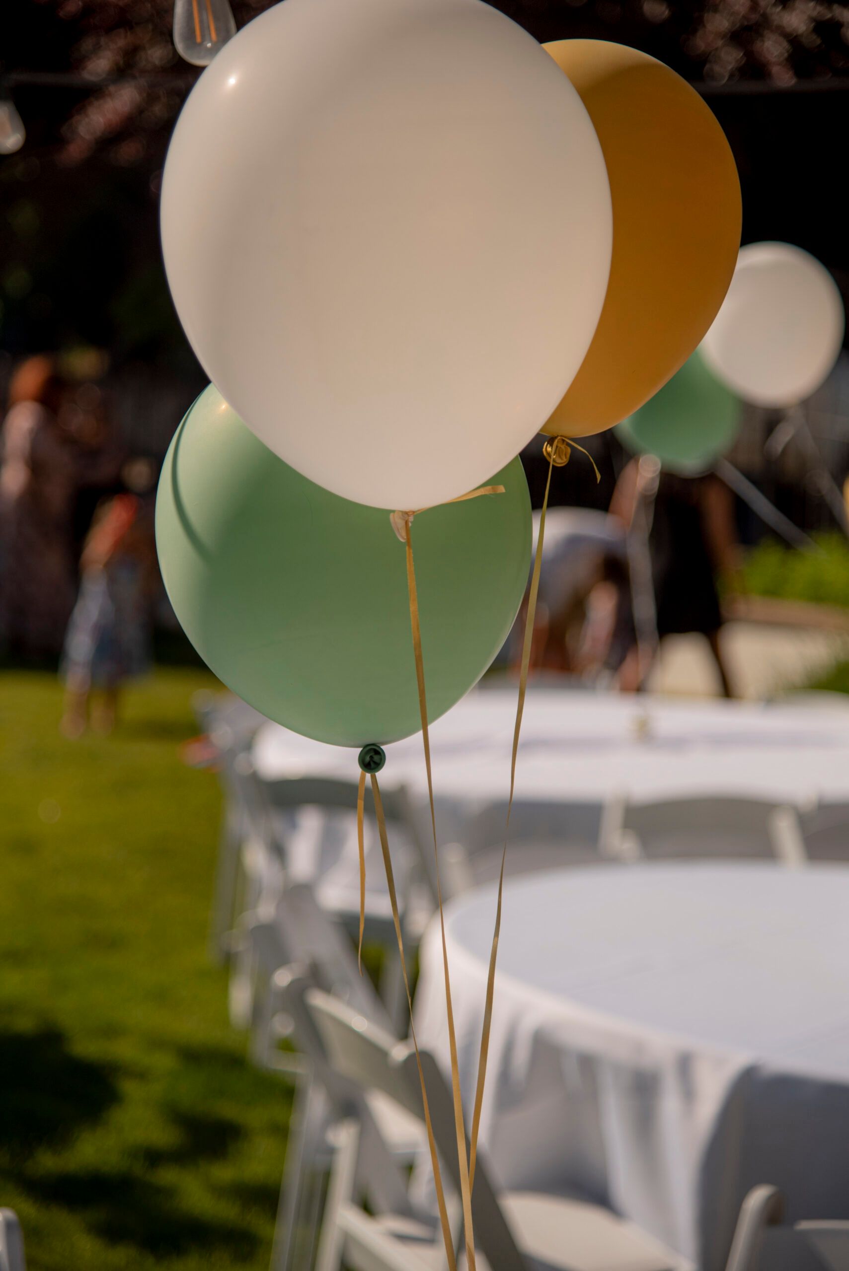 A bunch of balloons are hanging from a string in front of tables and chairs.